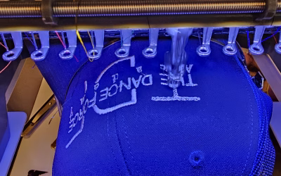 Embroidery machine stitching a white design onto a blue mesh-back cap